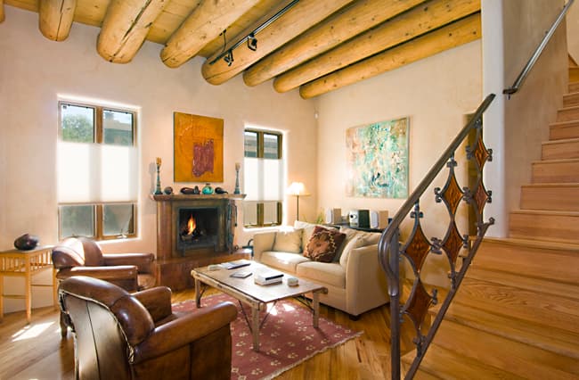 Sunlit Dancing Sun living room with exposed wooden vigas, fireplace, comfortable seating and staircase