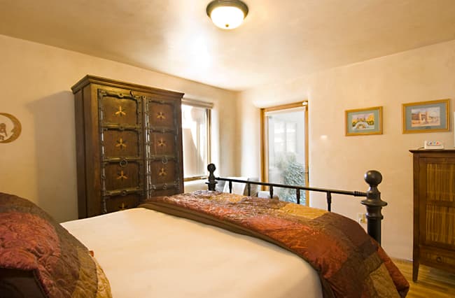 Second downstairs queen bedroom with wooden armoire and sunlight through two windows